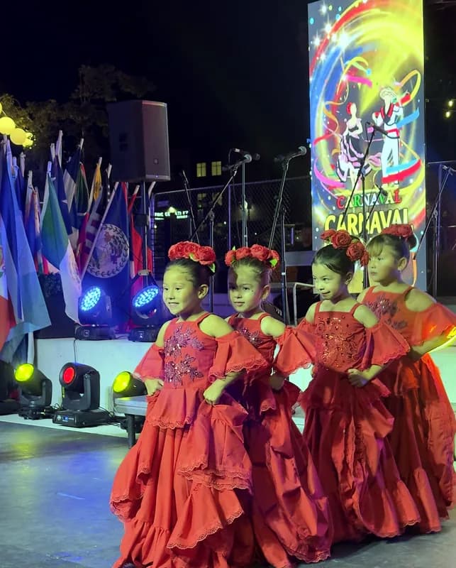 Cuatro niñas con pollera roja y flores en el cabello posan en el escenario frente al cartel del Carnaval de Barranquilla Utah.