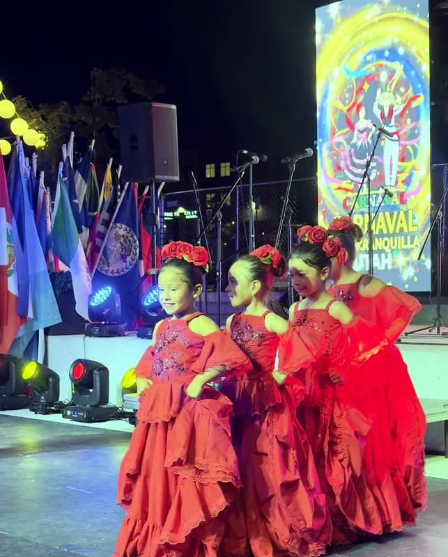 Una niña hace girar su pollera roja mientras sus compañeras la miran, con las banderas del festival al fondo.