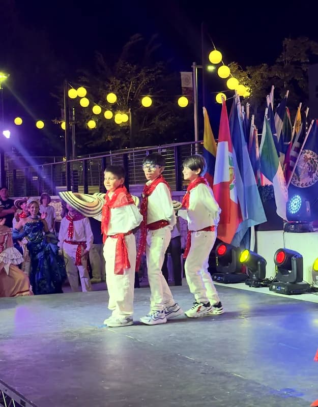 Tres niños con camisa blanca, pañoleta roja y sombrero vueltiao en la mano marcan el paso sobre el escenario.