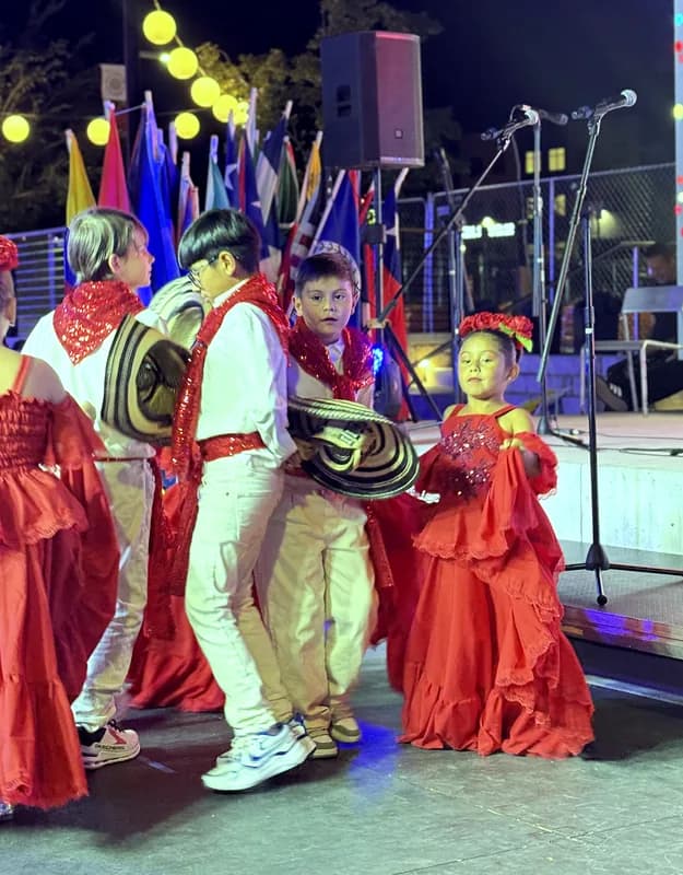 Niños con sombrero vueltiao y niñas con pollera roja bailan en pareja bajo las luces del escenario.