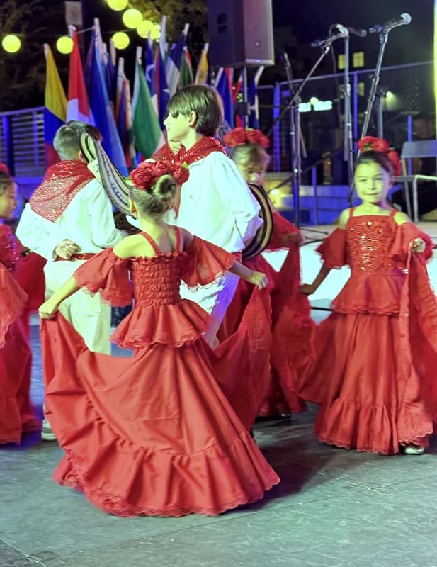 Una niña abre su pollera roja en pleno giro, entre un niño con sombrero y otra bailarina.