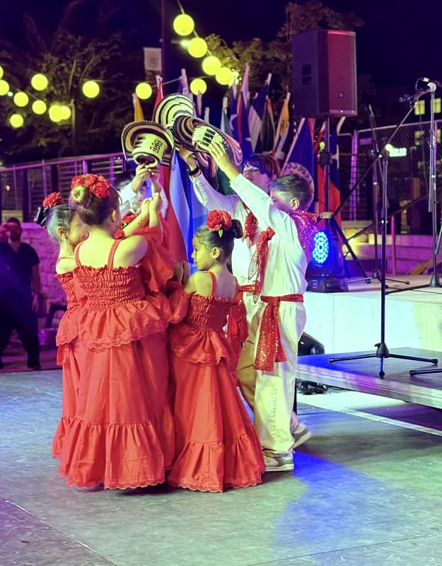 Un niño levanta dos sombreros vueltiaos sobre las bailarinas de pollera roja durante la coreografía.