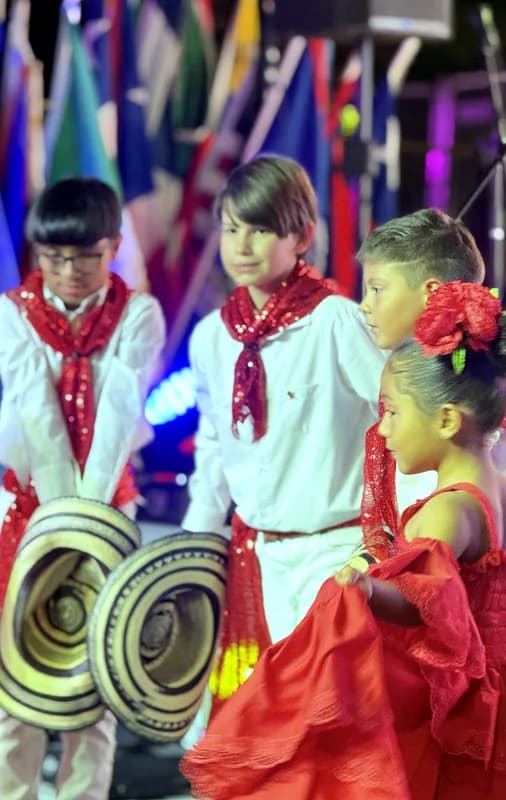 Primer plano de tres niños con pañoleta roja y sombreros vueltiaos junto a una niña con flores en el cabello.