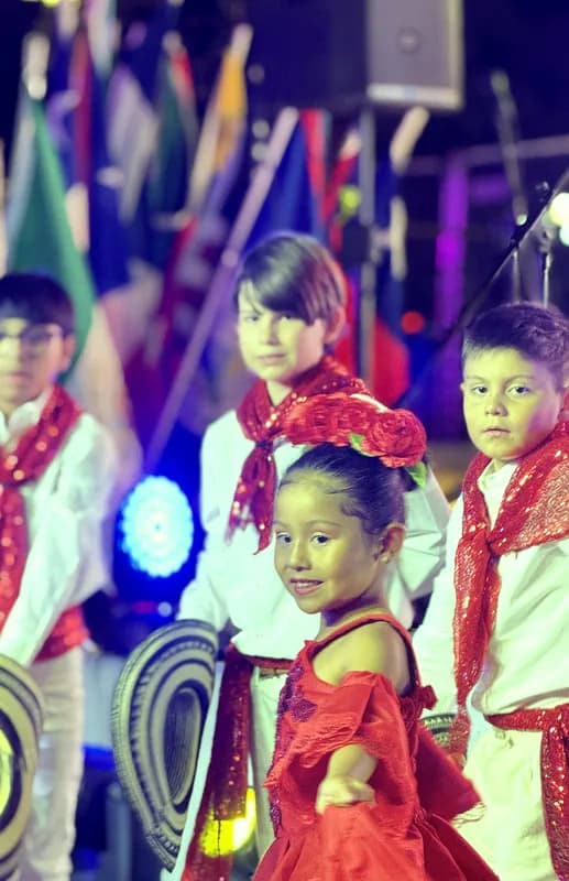 Una niña sonríe a la cámara sosteniendo su pollera roja, con dos niños de sombrero vueltiao detrás.