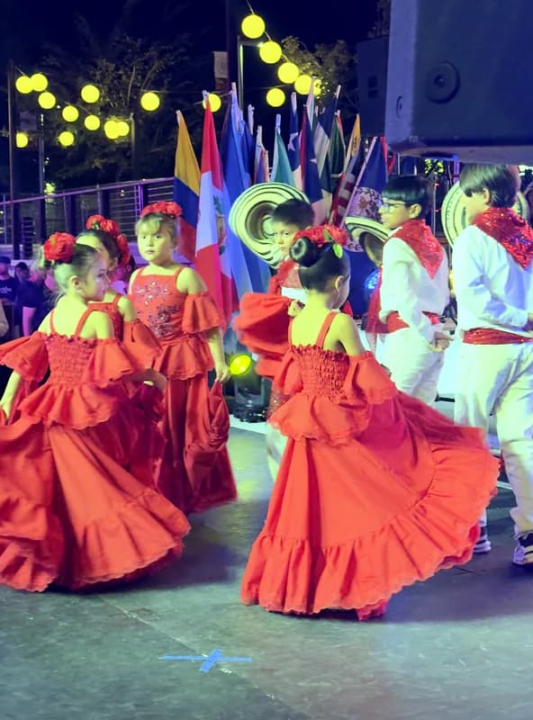 Dos niñas giran sus polleras rojas al mismo tiempo mientras los niños esperan con los sombreros en la mano.