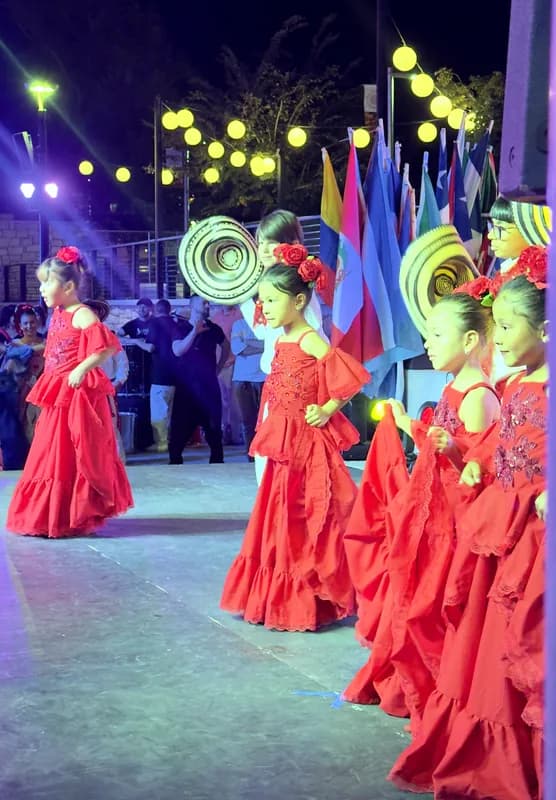Vista amplia del escenario al aire libre: las bailarinas en fila con sus polleras rojas bajo las luces del festival.